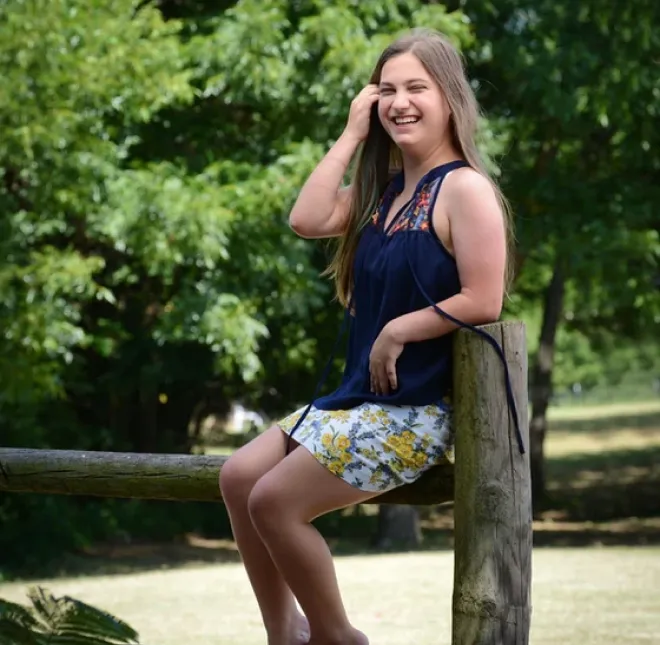 Young woman sitting on wooden fence