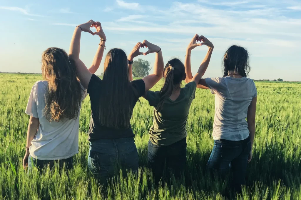 Women standing in field with hands forming love hearts