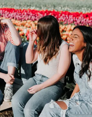 3 young women sitting down with rows of flowers behind